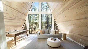 A cozy room with a wooden sloped ceiling, a sofa, a round ottoman, and a table with a board game.