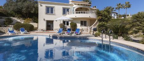A two-story building with a swimming pool, blue lounge chairs, and a balcony.