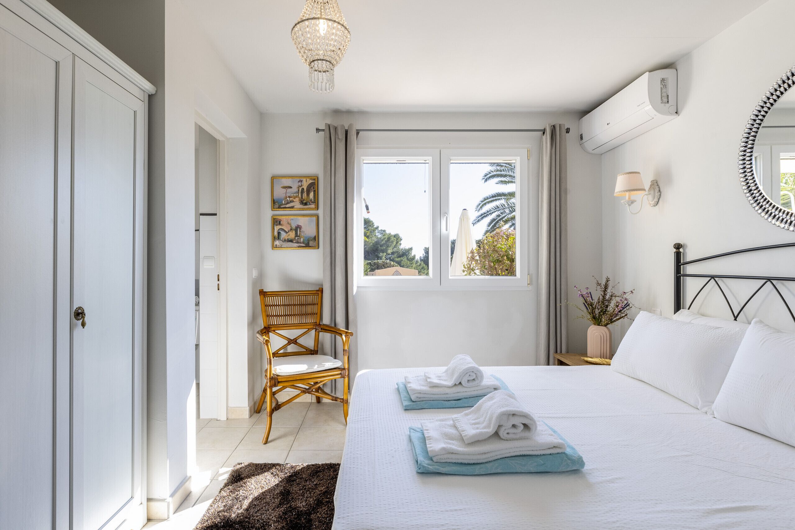 A bedroom with a bed, a chair, a window, and a wall-mounted air conditioner.