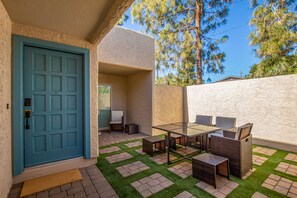 Une terrasse avec une porte bleue, des meubles en osier et une table en verre.