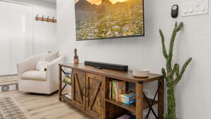 A modern living room with a large painting, a cactus plant, a wooden console table with books, and a white armchair.