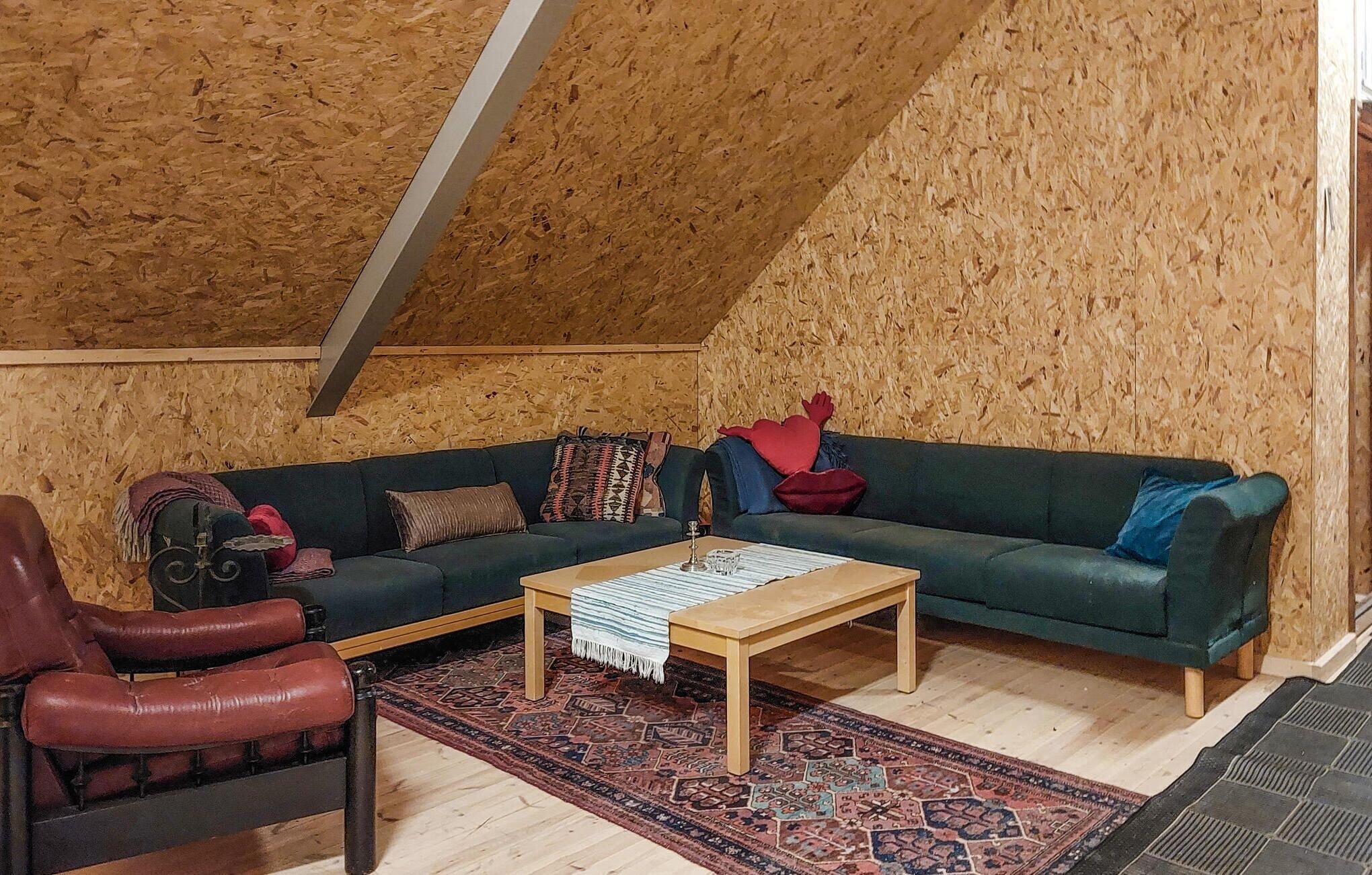 A loft-style room with a sloped ceiling, a dark green sofa, a wooden coffee table, and a patterned rug.