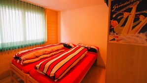 A single bed with striped bedding in a room with wooden walls and a window with sheer curtains. - Outside : Modern apartment  for 5 people, balcony-terrace, beautiful south view, located at tne entr (St-Luc)