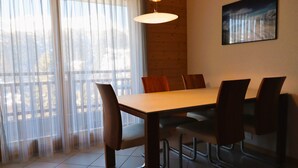 A dining area with a wooden table and chairs, large windows with sheer curtains, and a painting on the wall. - Outside : Modern apartment  for 5 people, balcony-terrace, beautiful south view, located at tne entr (St-Luc)