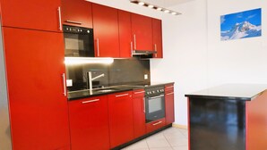 A kitchen with red cabinets, stainless steel appliances, and a black countertop. - Outside : Modern apartment  for 5 people, balcony-terrace, beautiful south view, located at tne entr (St-Luc)
