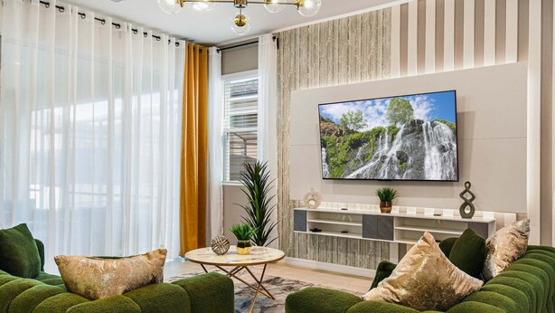 Sala de estar moderna com uma televisão grande, sofás verdes, uma mesa de centro e vista para uma cachoeira pela janela.