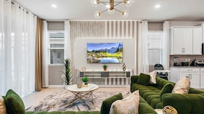 A modern living room with a large flat-screen TV, green upholstered sofa, and a marble-patterned rug. - Jurassic w Slide & Frozen-Themed/7BR @ Solara! (Kissimmee)