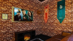 A room with a brick wall, a fireplace, a framed poster, and two banners. - Jurassic w Slide & Frozen-Themed/7BR @ Solara! (Kissimmee)