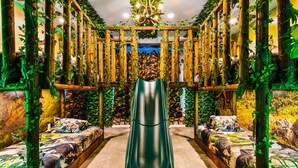 A room with a central slide, wooden pillars with ivy, and dinosaur-themed bedding.