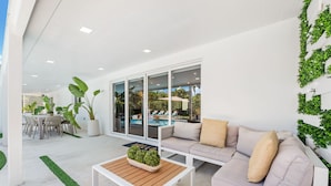 A modern outdoor living area with a white sofa, a wooden coffee table, and a dining set.