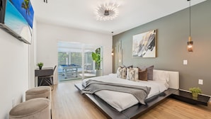 A modern bedroom with a large bed, a desk, and a view of the outdoors.