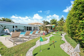 Un espace piscine avec des chaises longues et un petit terrain d’entraînement au putting.