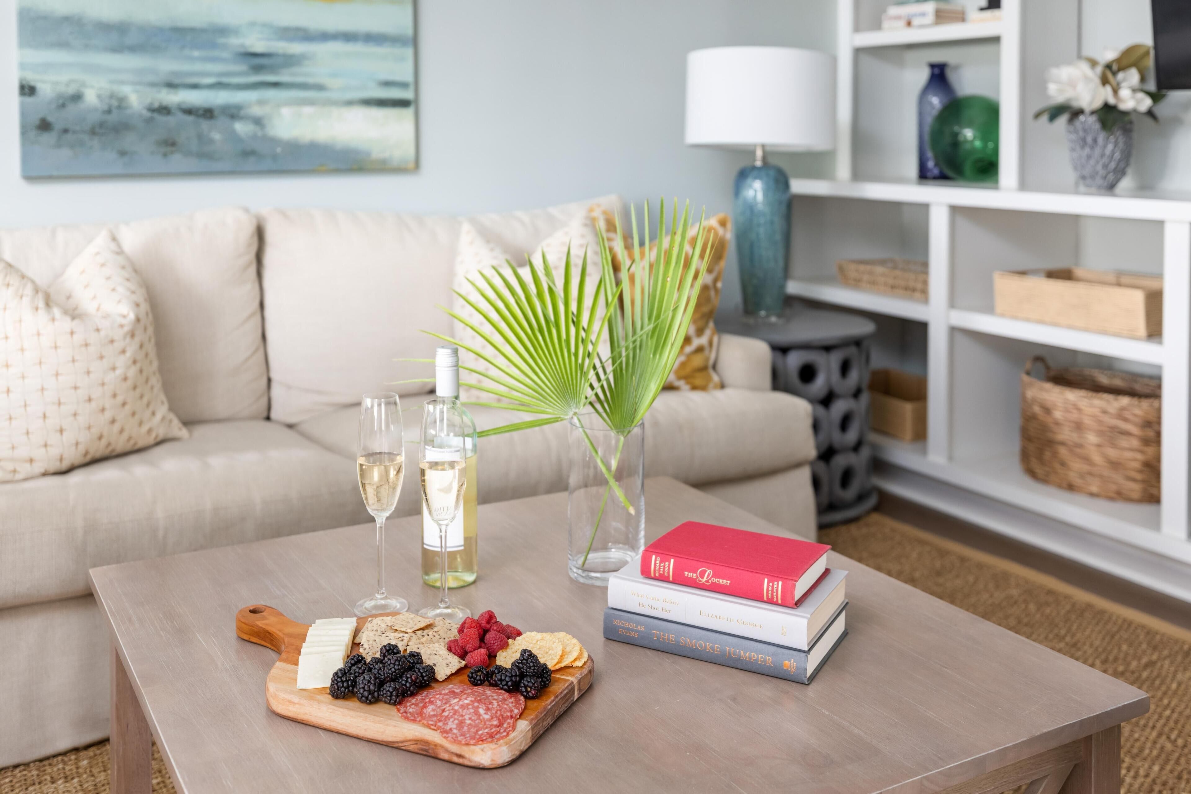 A living room with a wooden coffee table holding a charcuterie board, a glass of white wine, and a book titled "The Poisoner".