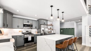 A modern kitchen with grey cabinets, stainless steel appliances, a marble island, and bar stools. - Lux canalfront home. Firepit, kayaks,paddleboat, 20 foot dock, chefs kitchen! (Houghton Lake)