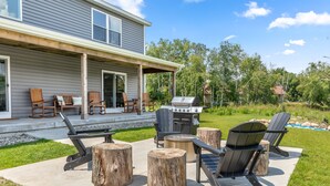 An outdoor patio with Adirondack chairs, a grill, and a concrete deck. - Lux canalfront home. Firepit, kayaks,paddleboat, 20 foot dock, chefs kitchen! (Houghton Lake)