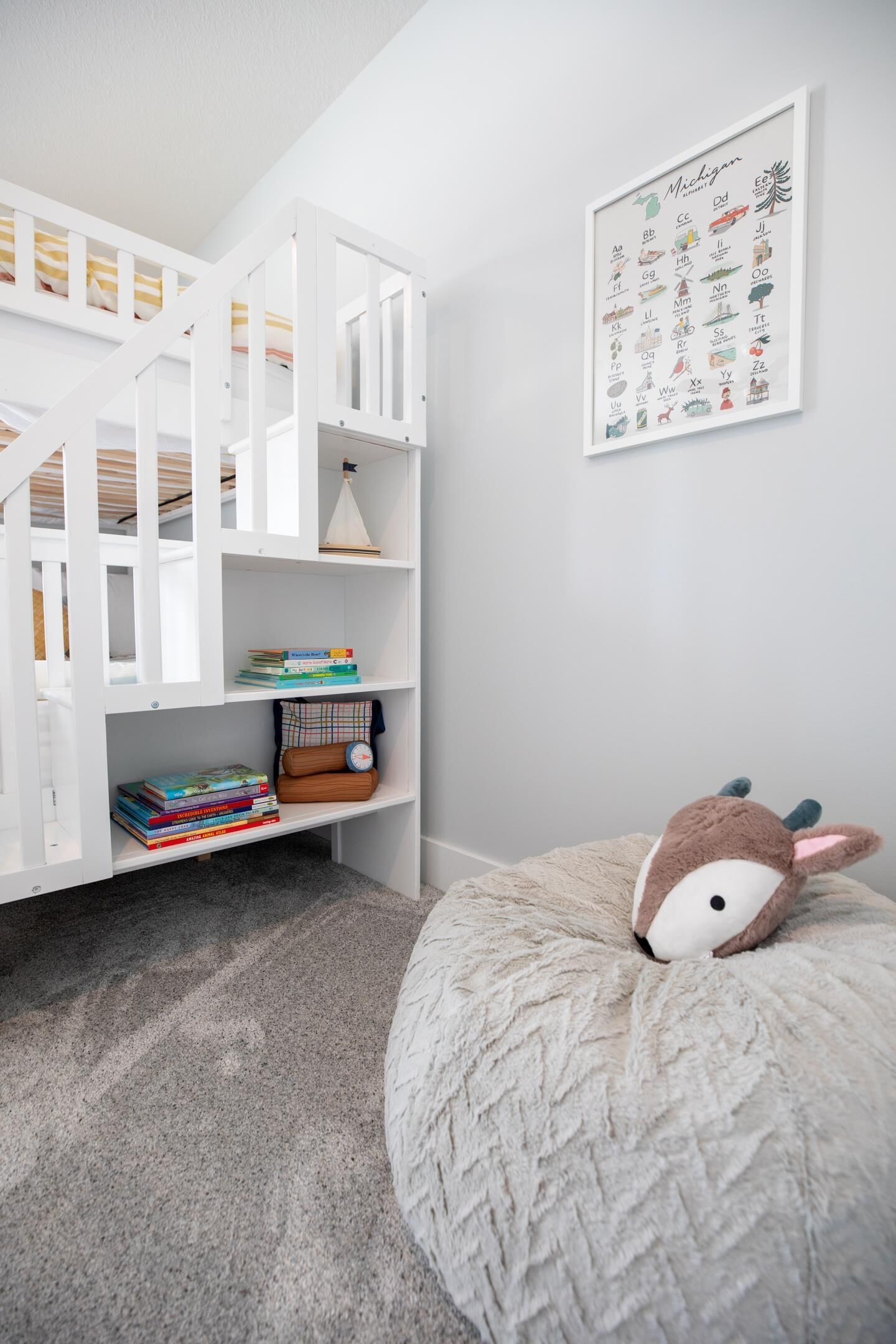 Une chambre d’enfant avec un lit superposé, une bibliothèque, un jouet en peluche et un tableau illustrant l’alphabet, accroché au mur.