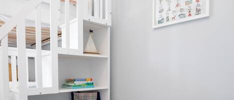 Une chambre d’enfant avec un lit superposé, une bibliothèque, un jouet en peluche et un tableau illustrant l’alphabet, accroché au mur.