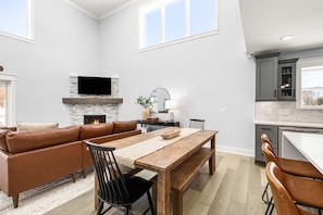 Ein modernes Wohnzimmer mit Kamin, Flachbildfernseher und Essbereich mit Holztisch und Stühlen.