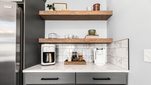 A kitchen with a stainless steel refrigerator, wooden shelves, a coffee maker, and a marble backsplash. - Lux canalfront home. Firepit, kayaks,paddleboat, 20 foot dock, chefs kitchen! (Houghton Lake)