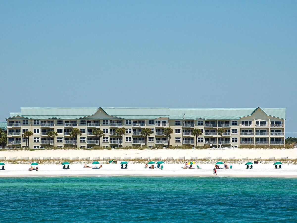 Ein Strandhotel mit mehreren Balkonen, einem Sandstrand und einem klaren, blauen Meer.