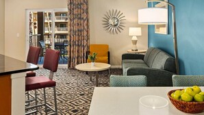 Habitación de hotel con zona de comedor, sofá, lámpara y vistas al balcón exterior.