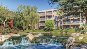 Un hotel con jardín ajardinado, un estanque con cascada y varios balcones.