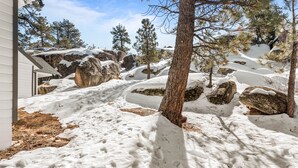 Un paisaje nevado con rocas grandes y árboles, un edificio blanco y un cielo despejado.