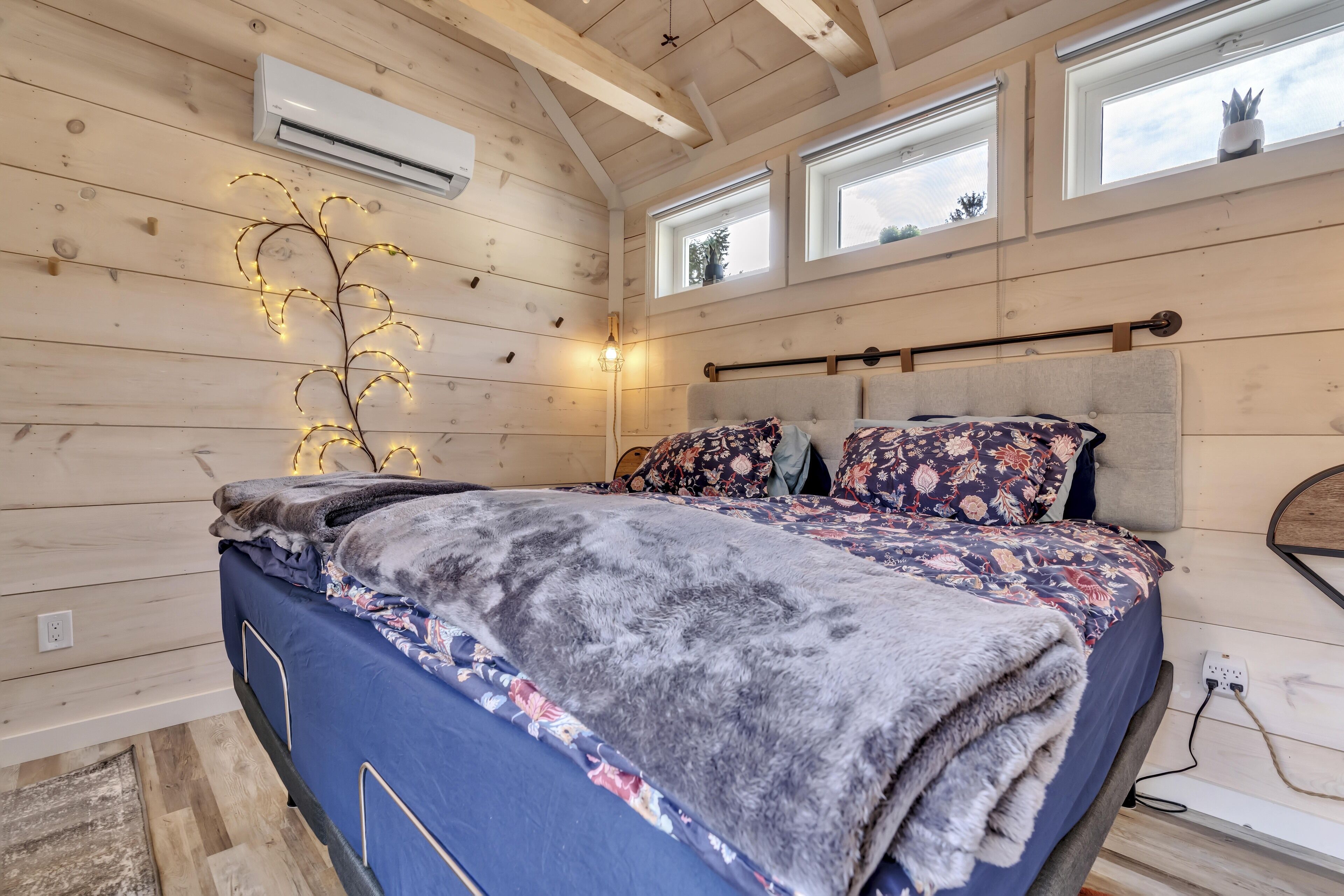 Ein Schlafzimmer mit Bett, Holzwänden, einer Klimaanlage und Fenstern.