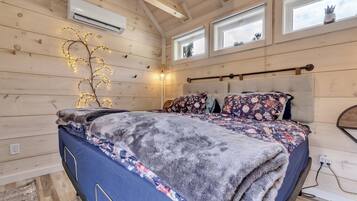 Ein Schlafzimmer mit Bett, Holzwänden, einer Klimaanlage und Fenstern.