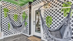 A room with a wooden floor, a white door, and two hammocks hanging from a white lattice wall. - Welcome to the Z E N (Acton)