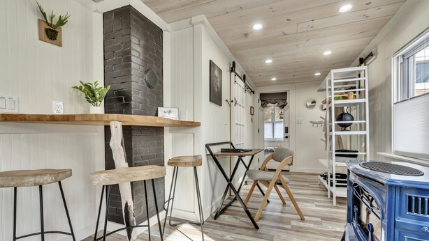 A cozy kitchen with wooden flooring, a brick wall, and a blue stove. There are bar stools and a small table with chairs. - Welcome to the Z E N (Acton)