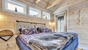 A cozy bedroom with a large bed, wooden walls, and multiple windows. - Welcome to the Z E N (Acton)