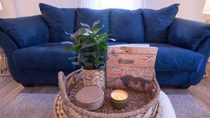 Ein blaues Sofa, ein Korbtablett mit einer Kerze, ein Willkommensschild und eine Pflanze.