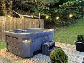 Een hottub op een houten terras met een houten omheining en sfeerverlichting op de achtergrond.