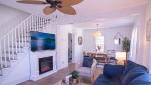 Ein modernes Wohnzimmer mit Kamin, einem großen Flachbildfernseher, einem blauen Sofa und einem Essbereich mit Tisch und Stühlen.