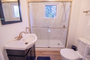 Een badkamer met een douche, wastafel, toilet en een spiegel.