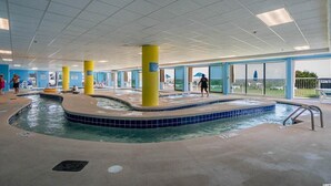Une piscine intérieure avec des piliers jaunes, des carreaux bleu clair et une vue sur l’extérieur.