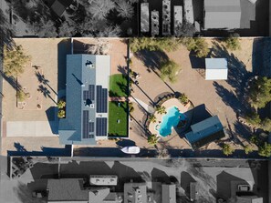 Vue aérienne d’un quartier résidentiel avec une piscine, des panneaux solaires et un petit jardin.
