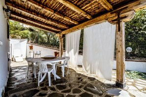 An outdoor patio with a stone floor, a wooden pergola, white curtains, and a table with chairs. - Casa Vacanza La Collinetta | 2 bedrooms, 2 bathrooms, porch (budoni)