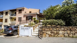 A multi-story residential building with a stone wall and a car parked in front. - Casa Vacanza La Collinetta | 2 bedroom, 2 baths, veranda (budoni)