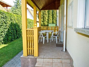 Un patio cubierto con una mesa y sillas, cerca de una valla de madera y un seto verde.