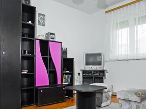 Una sala de estar con televisor, un mueble rosa y negro, y una mesita.