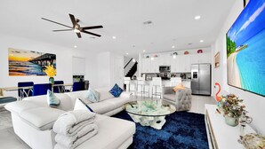 A modern living room with a white sofa, a glass coffee table, and a blue rug. - Amped at Reunion | 4BR Home w Private Pool, Theater, Themed Kids' Room, and Arcade Near Disney (Kissimmee)