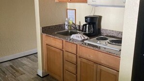 A small kitchen with wooden cabinets, a microwave, a coffee maker, and a sink. - Dunedin Condo on the Water (Dunedin)