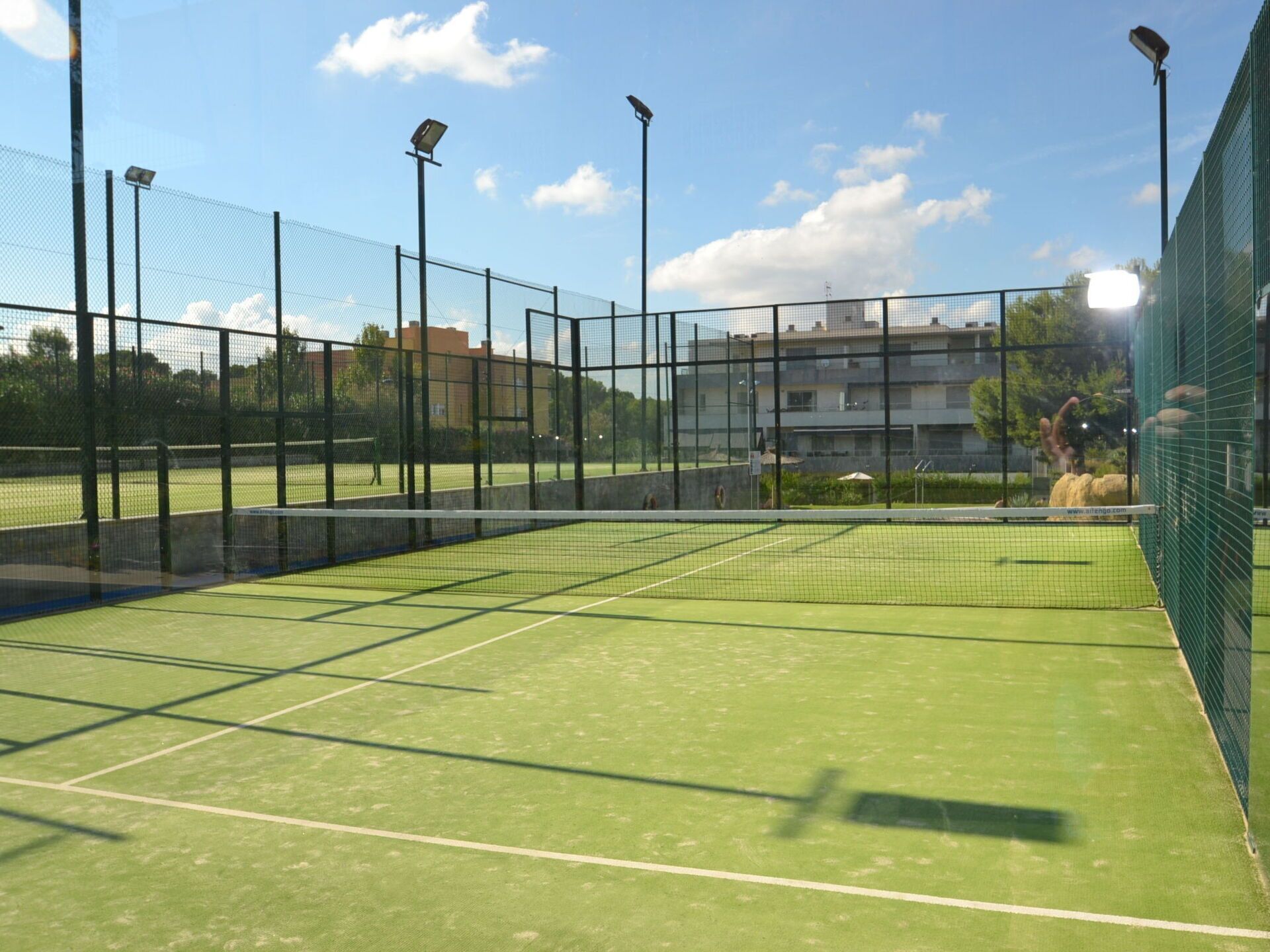 Un court de tennis avec un filet, entouré d’une clôture et éclairé par des lampadaires.