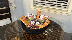 Ein Esstisch mit Glasplatte, eine Korb mit verschiedenen Snacks und ein Holzstuhl.