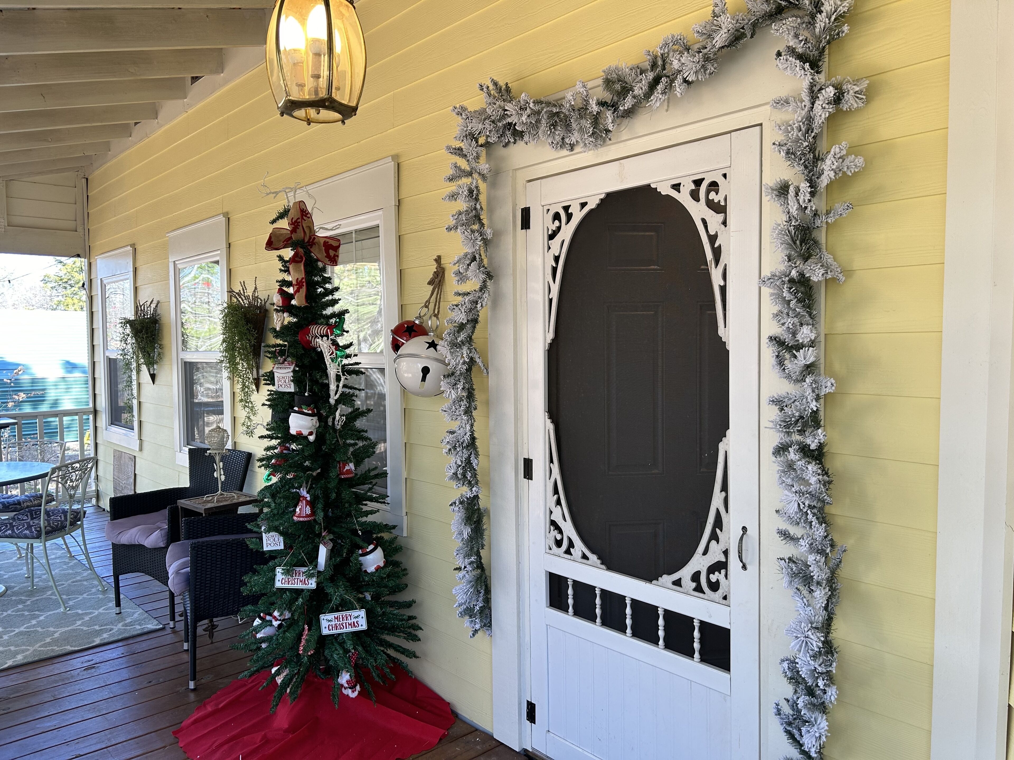 A porch with a Christmas tree, a white door with decorative trim, and a hanging lantern.