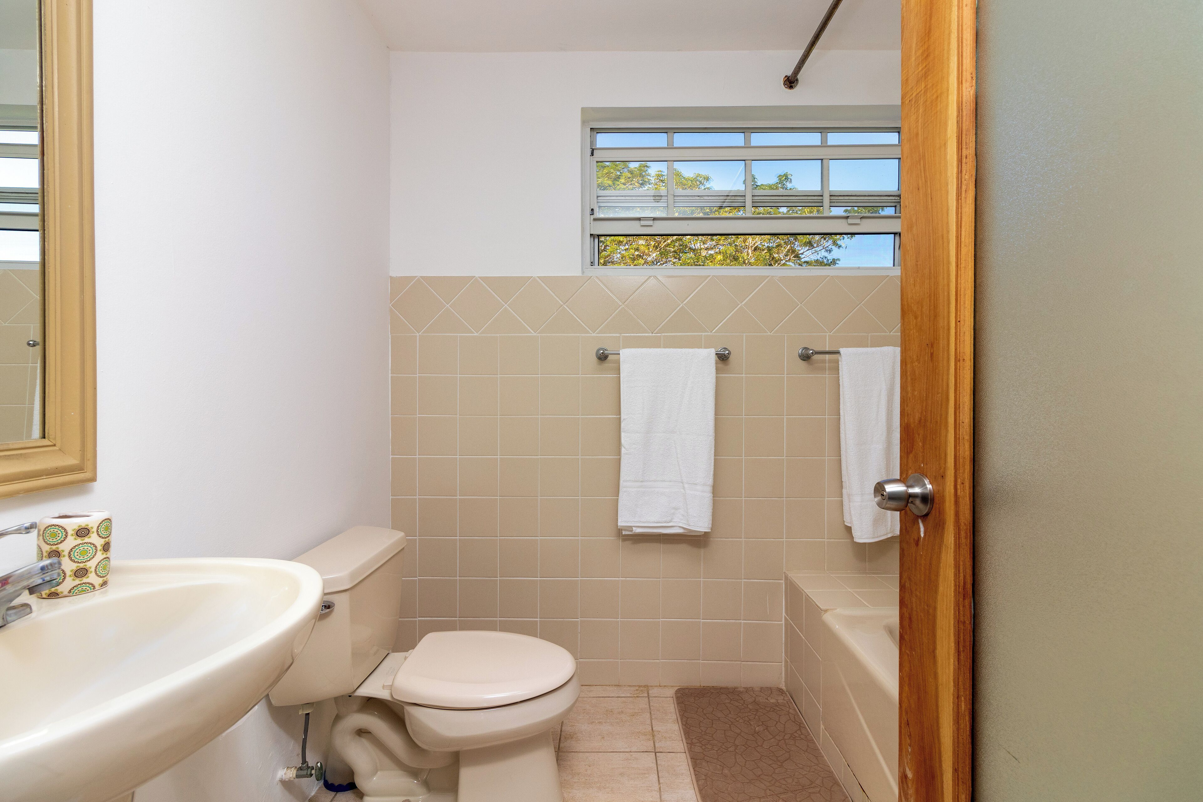 A bathroom with a toilet, sink, and bathtub. There is a window above the bathtub and a towel hanging on the wall.