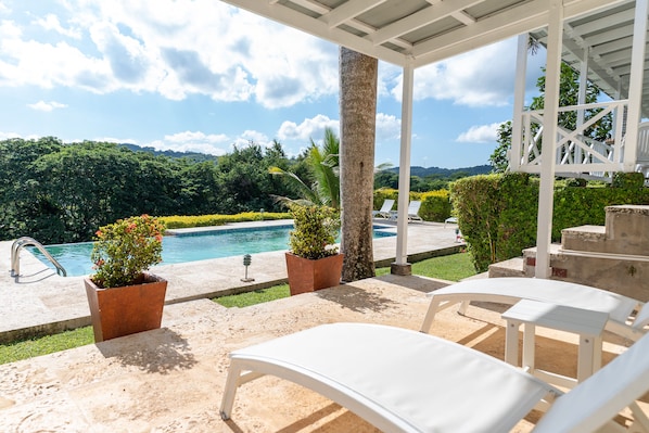 A covered outdoor area with a pool, lounge chairs, and potted plants.