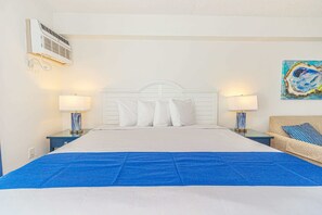 A hotel room with a large bed, two bedside tables with lamps, a wall-mounted air conditioner, and a painting on the wall.